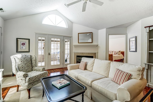 living room with a ceiling fan, wood finished floors, visible vents, lofted ceiling, and a tile fireplace