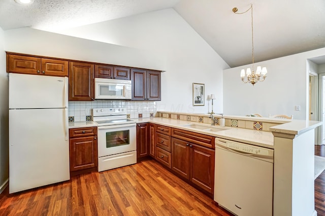 kitchen featuring white appliances, a peninsula, light countertops, and a sink