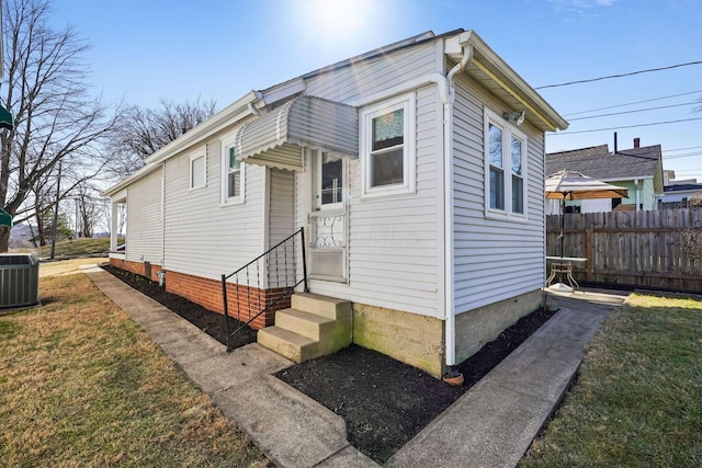 bungalow-style home with entry steps, a front yard, fence, and central AC