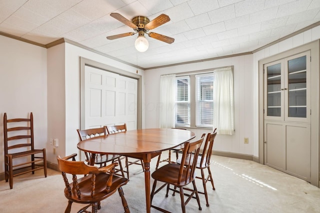 dining area featuring ceiling fan, light colored carpet, baseboards, and ornamental molding