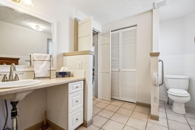 bathroom featuring tile walls, toilet, wainscoting, tile patterned floors, and a textured ceiling