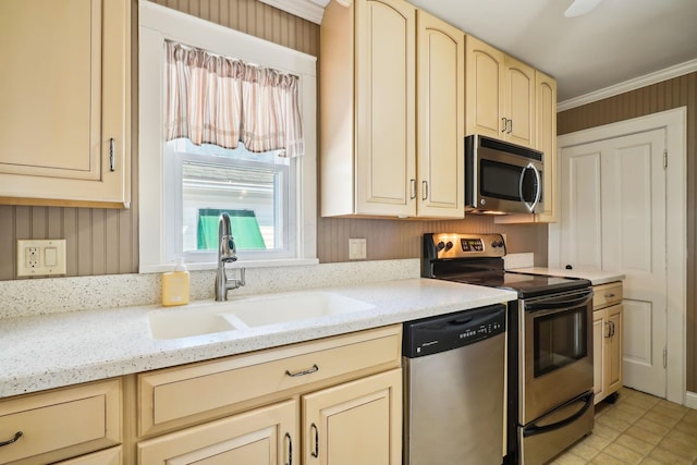 kitchen with cream cabinetry, ornamental molding, a sink, stainless steel appliances, and light stone countertops