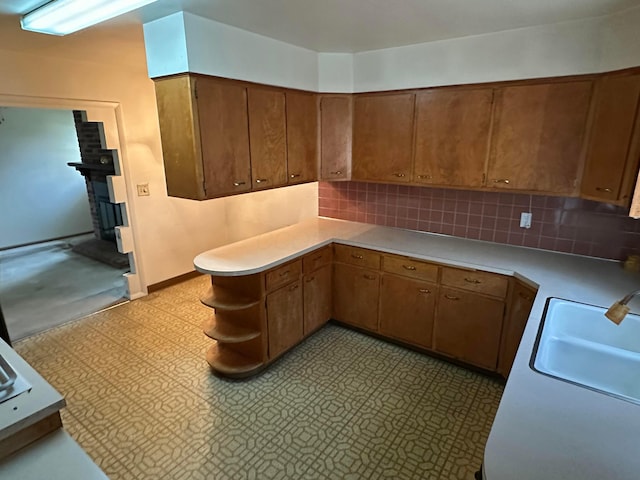 kitchen with brown cabinetry, light floors, a sink, light countertops, and tasteful backsplash