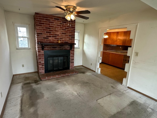 unfurnished living room featuring a brick fireplace, a ceiling fan, and baseboards