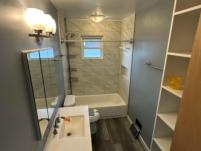 bathroom featuring visible vents, toilet, shower / tub combination, wood finished floors, and a sink