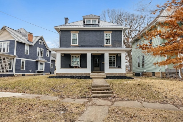 traditional style home with a front yard, covered porch, a chimney, brick siding, and metal roof