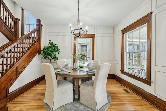 dining space with a decorative wall, baseboards, stairs, light wood-style flooring, and a notable chandelier