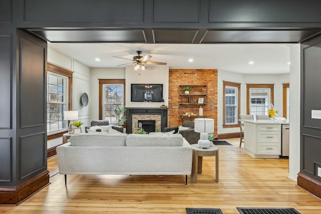 living room with recessed lighting, light wood-style floors, a stone fireplace, and a ceiling fan