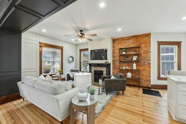 living area with a ceiling fan, recessed lighting, light wood-style floors, a fireplace, and a decorative wall