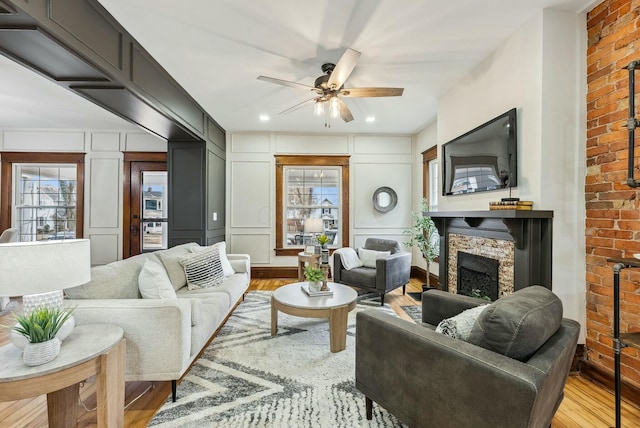 living area featuring a ceiling fan, wood finished floors, recessed lighting, a fireplace, and a decorative wall