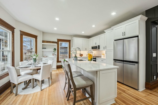 kitchen with light countertops, stainless steel appliances, light wood-style floors, white cabinetry, and a sink