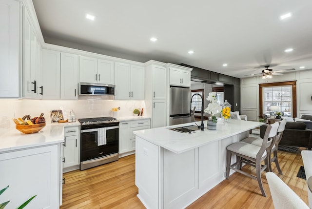 kitchen featuring a kitchen breakfast bar, appliances with stainless steel finishes, light wood-style floors, white cabinetry, and a sink