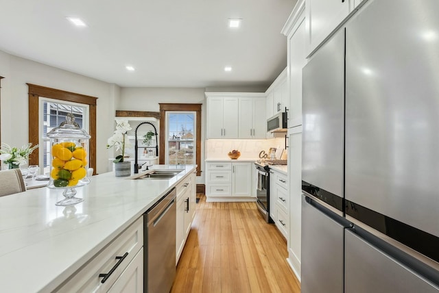 kitchen with light wood-type flooring, decorative backsplash, stainless steel appliances, white cabinetry, and a sink