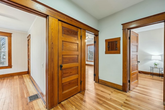 hall with visible vents, crown molding, light wood-type flooring, and baseboards