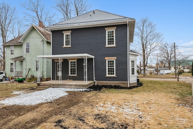 back of house featuring metal roof, brick siding, and covered porch