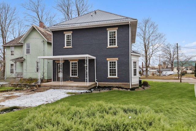 rear view of house with brick siding, covered porch, metal roof, and a yard