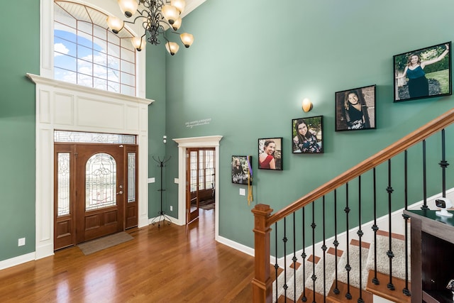 entryway with a notable chandelier, wood finished floors, a high ceiling, baseboards, and stairs