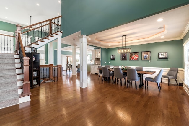 dining space with a raised ceiling, wood finished floors, and ornate columns