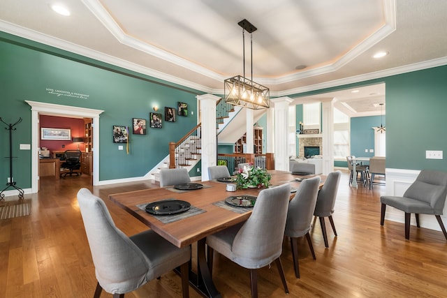 dining area featuring ornamental molding, wood finished floors, a raised ceiling, stairs, and ornate columns