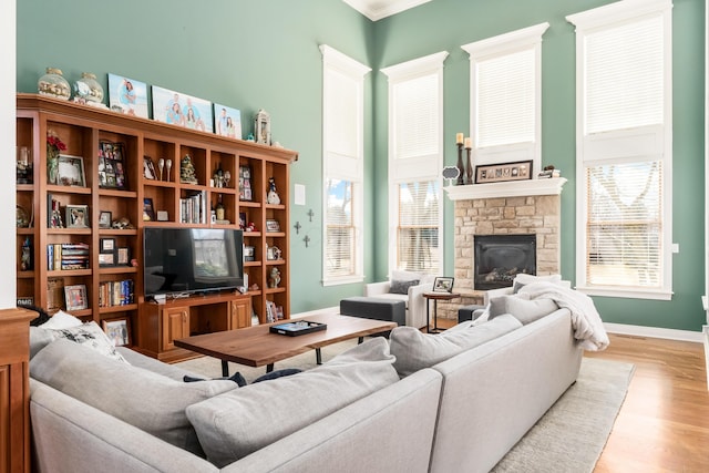 living area with a stone fireplace, ornamental molding, baseboards, and wood finished floors