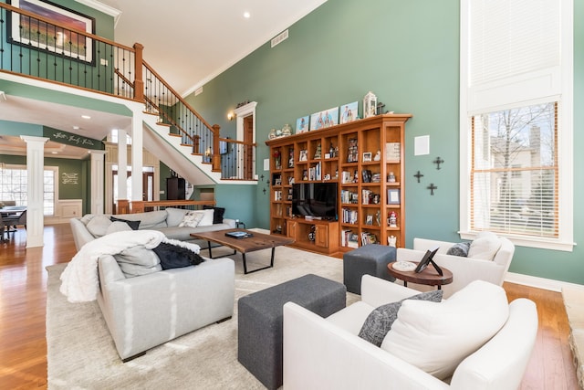 living room featuring wood finished floors, a towering ceiling, crown molding, and ornate columns