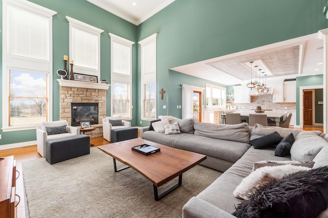 living room with baseboards, light wood-style flooring, a high ceiling, ornamental molding, and a stone fireplace