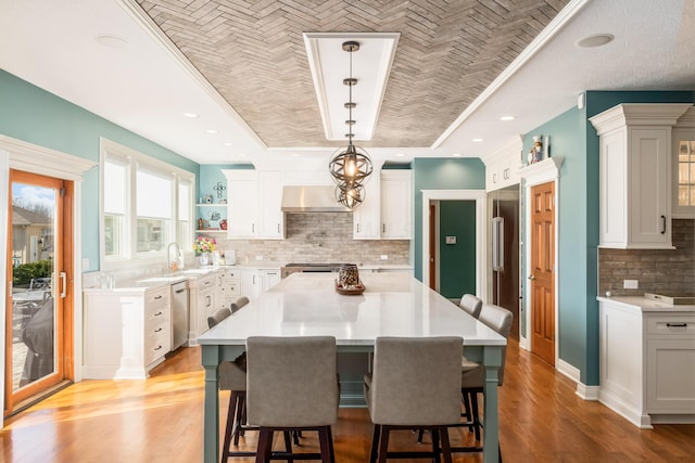 kitchen featuring a kitchen bar, light countertops, light wood-style floors, exhaust hood, and a raised ceiling