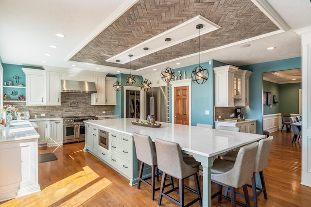 kitchen featuring crown molding, premium appliances, a large island, wall chimney exhaust hood, and a sink