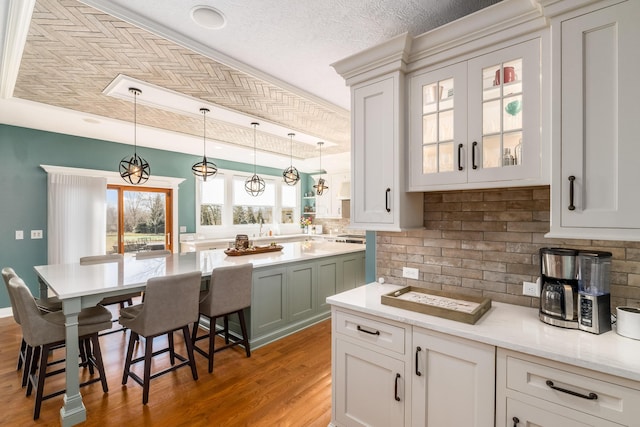 kitchen featuring light wood finished floors, backsplash, glass insert cabinets, pendant lighting, and a breakfast bar area