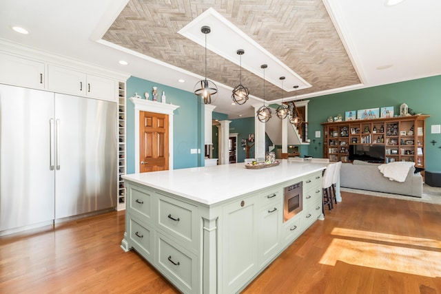 kitchen with a center island, built in appliances, light countertops, light wood-style floors, and hanging light fixtures