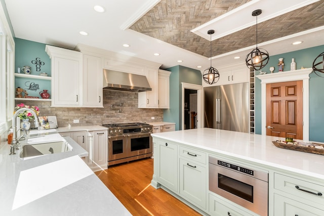 kitchen featuring high quality appliances, light countertops, hanging light fixtures, wall chimney exhaust hood, and a sink