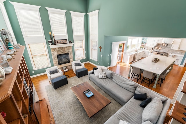 living area with a stone fireplace, light wood-style flooring, baseboards, and a towering ceiling