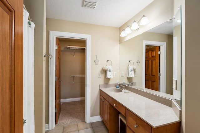 full bathroom with visible vents, a walk in closet, a textured ceiling, tile patterned flooring, and vanity