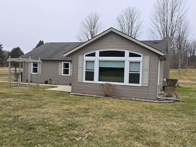 rear view of house with a patio, a lawn, roof with shingles, and a chimney