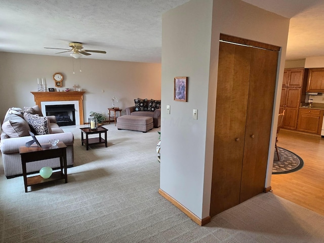 living area featuring baseboards, light carpet, a fireplace, a textured ceiling, and a ceiling fan