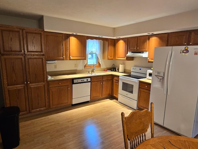 kitchen featuring light wood finished floors, under cabinet range hood, light countertops, white appliances, and a sink