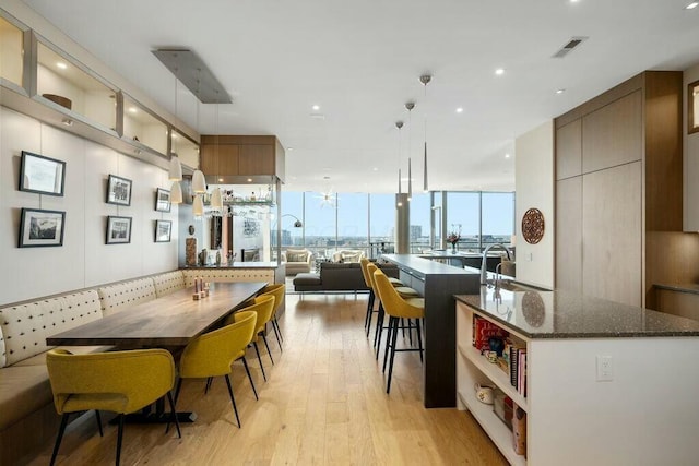 kitchen featuring visible vents, dark stone counters, an island with sink, light wood-style floors, and modern cabinets