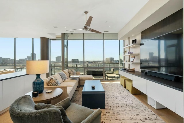 living room featuring a wall of windows, light wood-style floors, a city view, and ceiling fan