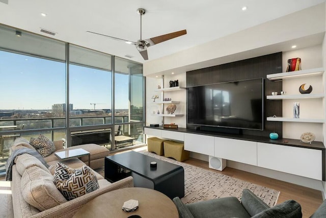 living room featuring ceiling fan, visible vents, wood finished floors, and floor to ceiling windows