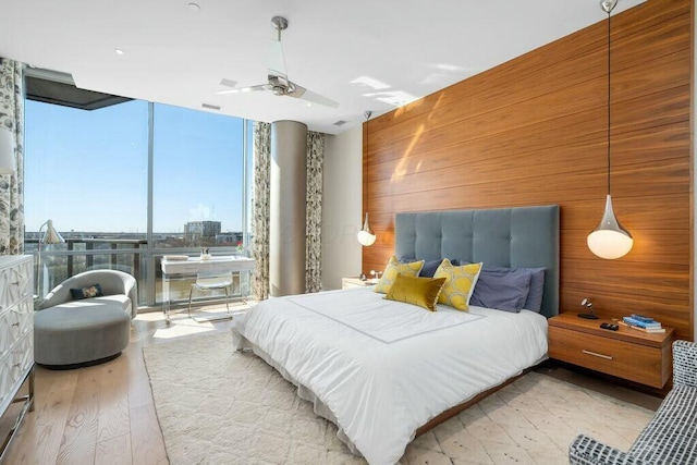 bedroom with visible vents, wood walls, expansive windows, wood finished floors, and a ceiling fan