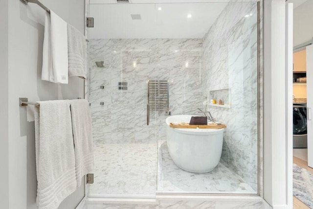 bathroom featuring a freestanding tub, marble finish floor, a marble finish shower, tile walls, and washer / dryer