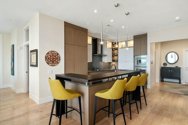 kitchen with dark countertops, modern cabinets, a breakfast bar area, and wall chimney range hood