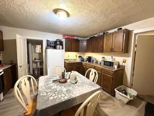 kitchen featuring freestanding refrigerator, a sink, dark brown cabinetry, light countertops, and a textured ceiling