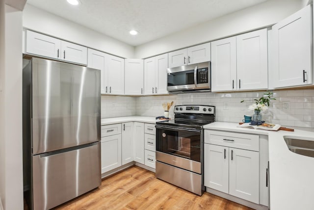 kitchen with backsplash, appliances with stainless steel finishes, light wood-style flooring, and light countertops