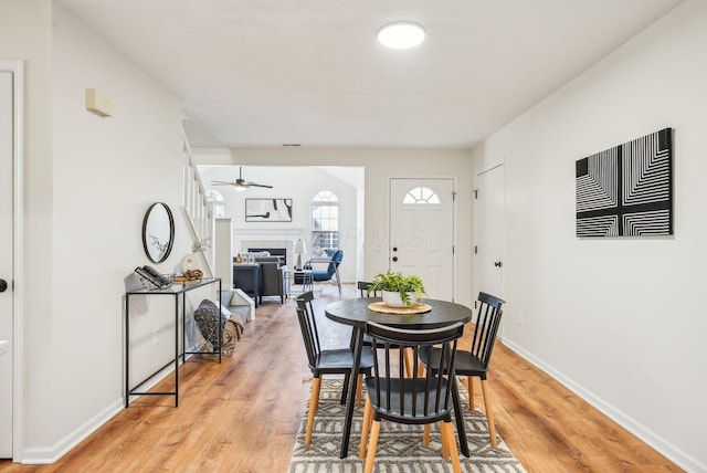 dining space featuring light wood-type flooring, baseboards, a ceiling fan, and a fireplace