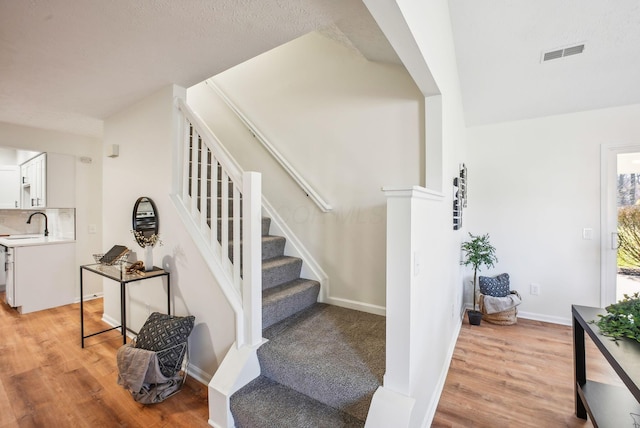 stairway featuring visible vents, baseboards, and wood finished floors