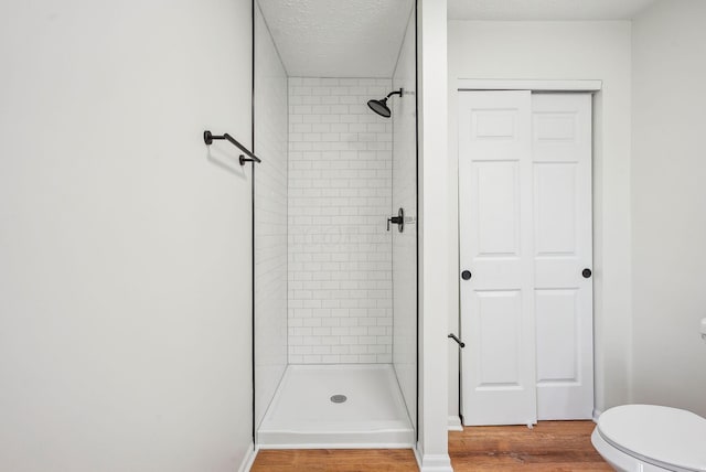 full bath with toilet, wood finished floors, a shower stall, and a textured ceiling