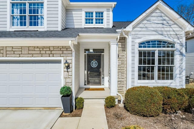 doorway to property featuring concrete driveway, a garage, stone siding, and a shingled roof