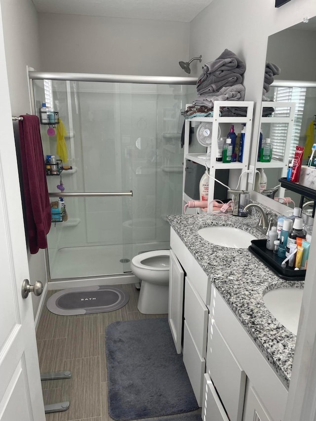 full bath featuring a sink, toilet, a stall shower, and double vanity