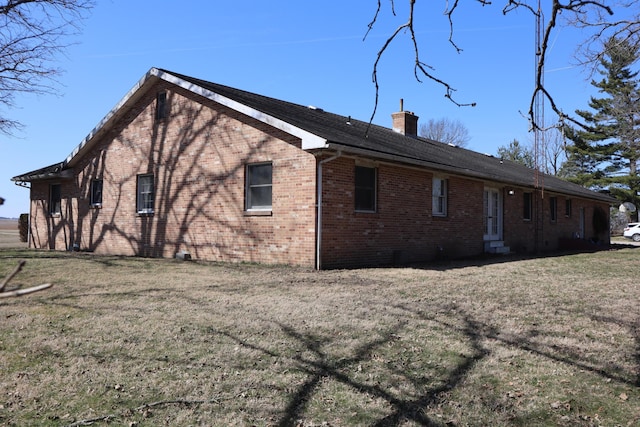 rear view of property with a yard, brick siding, and a chimney